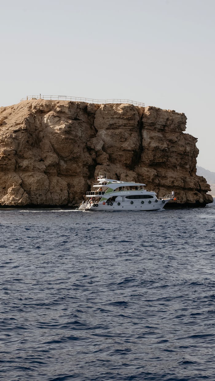A luxury yacht sails by the rocky cliffs of Sharm El-Sheikh, Egypt, capturing a serene coastal view.