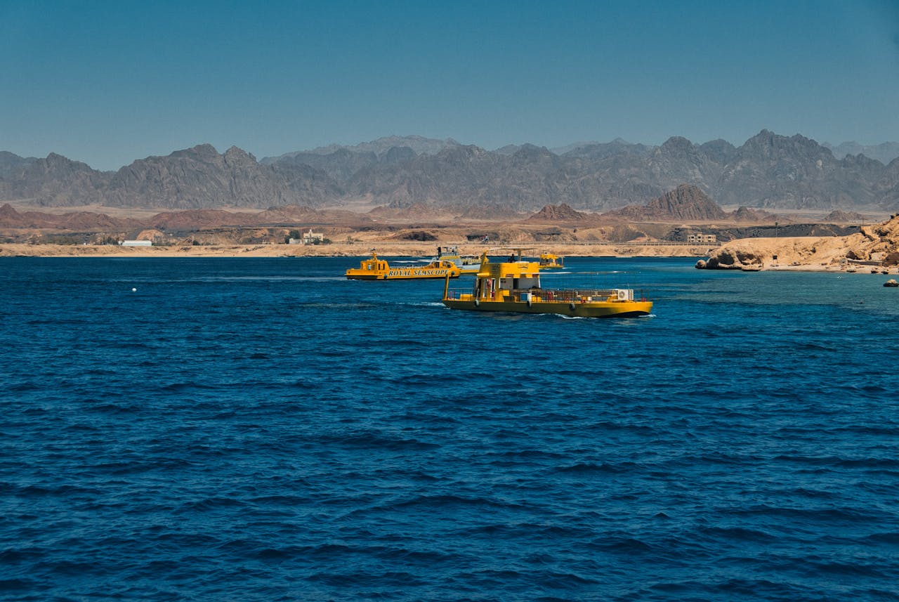Yellow boats float on the vibrant blue waters of Ras Mohammed with scenic Egyptian mountains in the background.